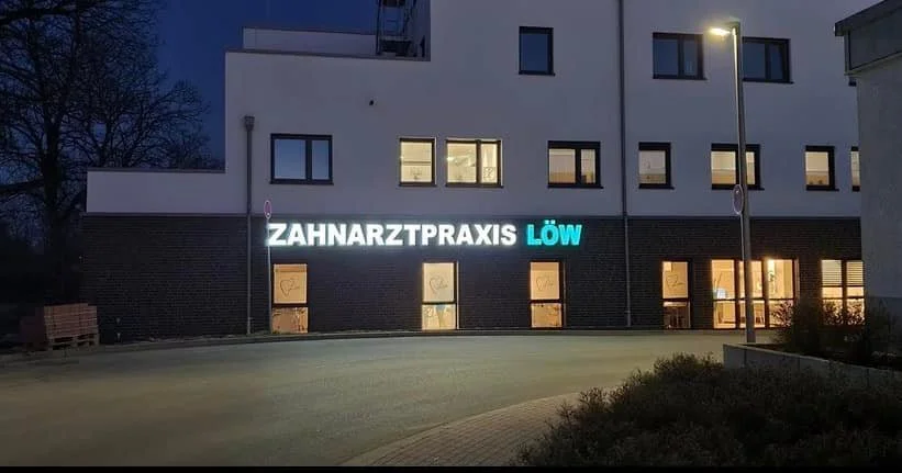 Beleuchteter Schriftzug Zahnarztpraxis Löw an einer Fassade bei Dämmerung