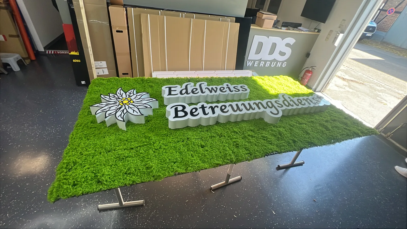 Edelweiss-Schriftzug mit Blütenmotiv auf einer Moosfläche in der DDS-Werkstatt