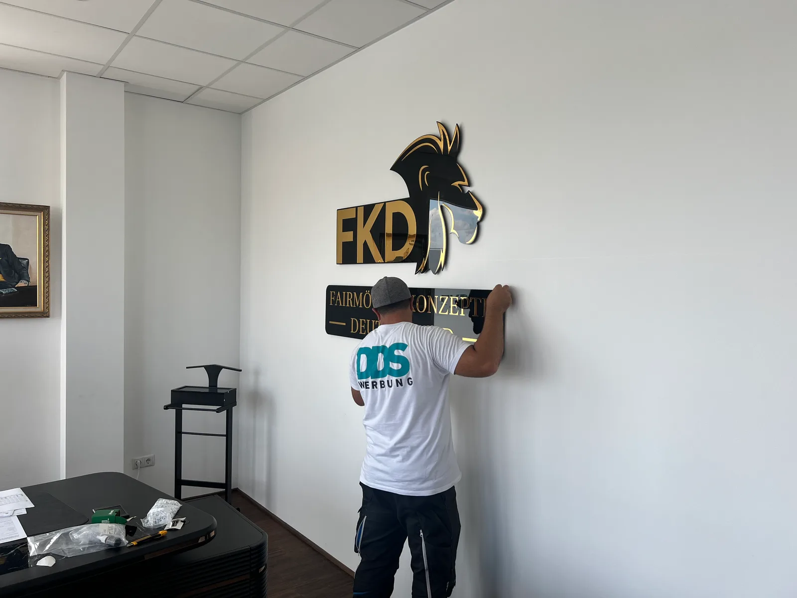 DDS-Mitarbeiter richtet einen Schriftzug unter dem FKD-Wandlogo aus