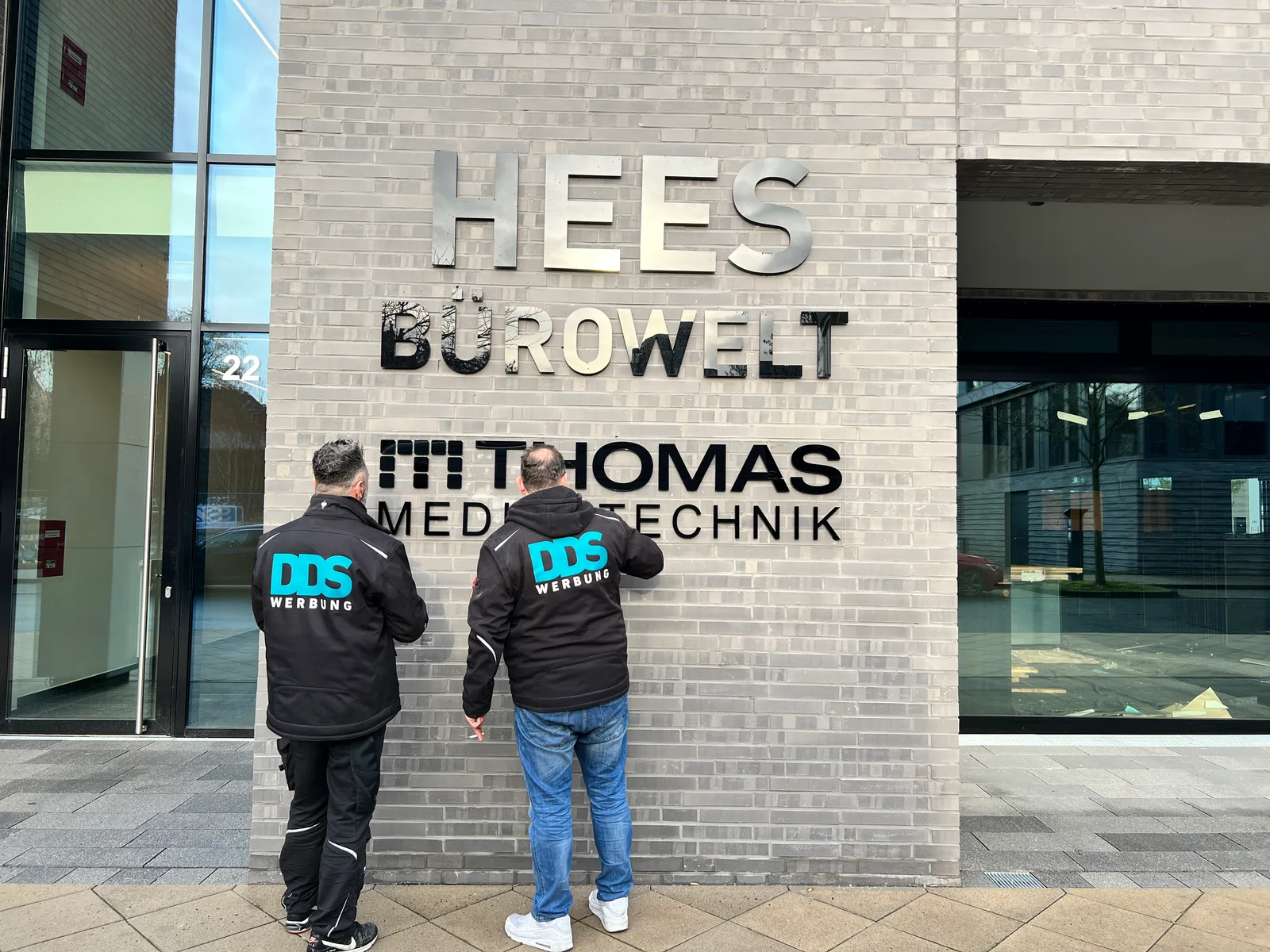 Zwei DDS-Mitarbeiter montieren den Schriftzug HEES Bürowelt an der Fassade