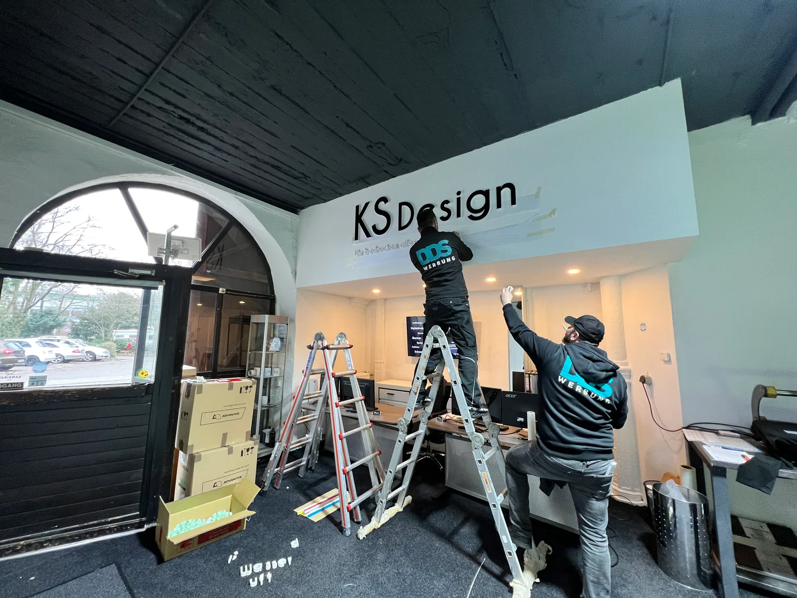 DDS-Team montiert den Schriftzug KS Design in einem Ausstellungsraum